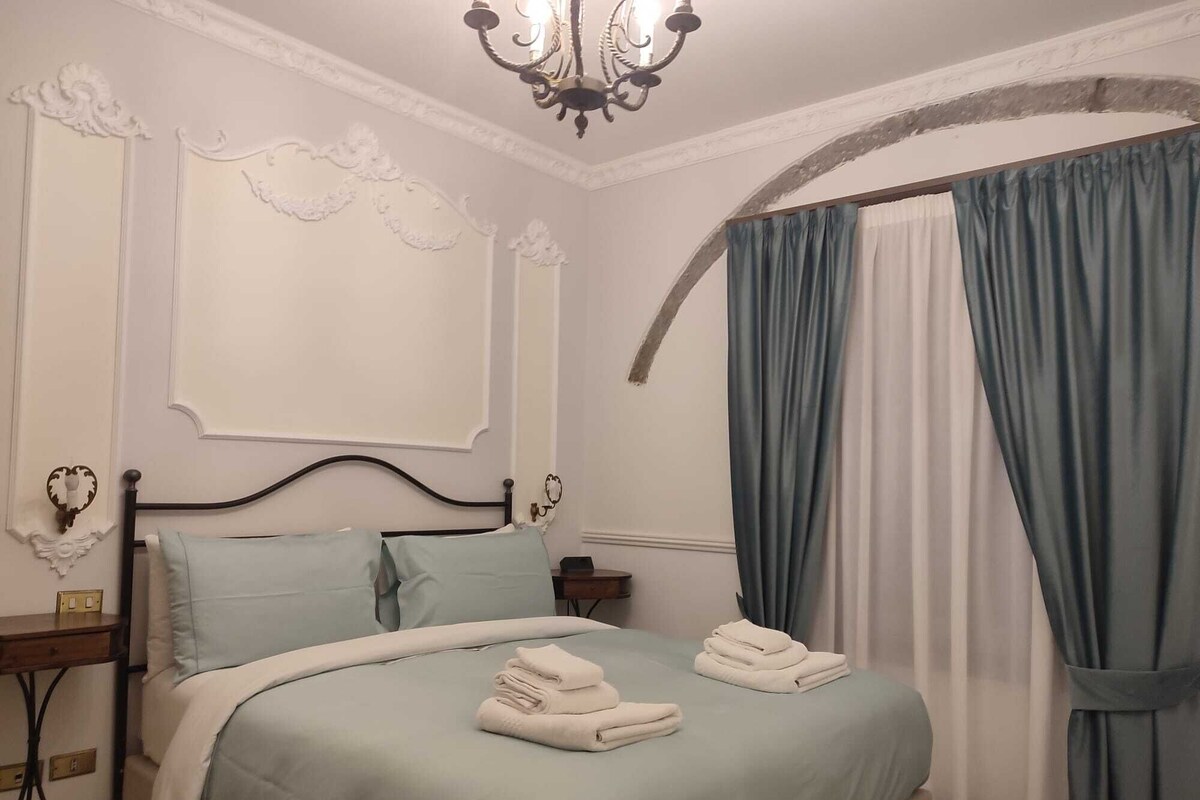 Un dormitorio con cama, mesita de noche, candelabro y cortinas.