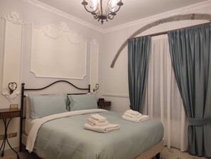 A bedroom with a bed, a nightstand, a chandelier, and curtains. - Carafa di Maddaloni B&B di Charme (Naples)