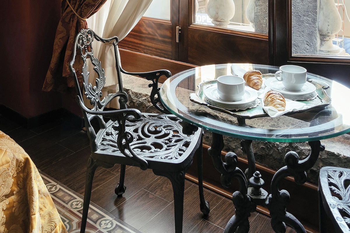 Una habitación con una mesa de comedor preparada para dos personas, una silla y vistas a un balcón exterior con detalles arquitectónicos.