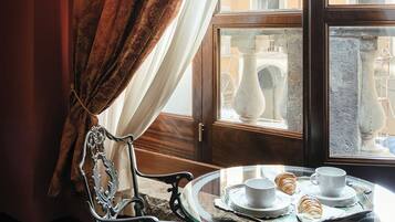 Una stanza con un tavolo da pranzo apparecchiato per due persone, una sedia e vista su un balcone esterno con elementi architettonici.