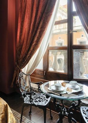 Una habitación con una mesa de comedor preparada para dos personas, una silla y vistas a un balcón exterior con detalles arquitectónicos.