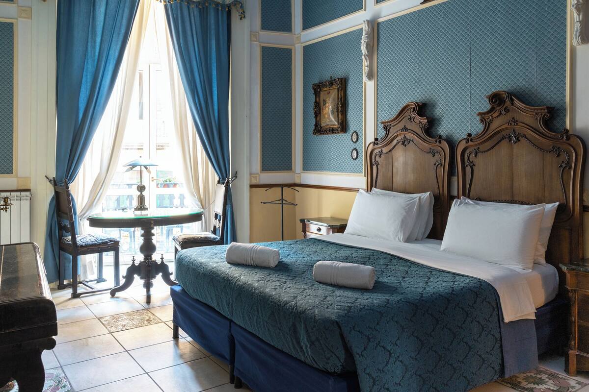 Un dormitorio con una cama grande, una mesita de noche, una silla y una ventana con cortinas.