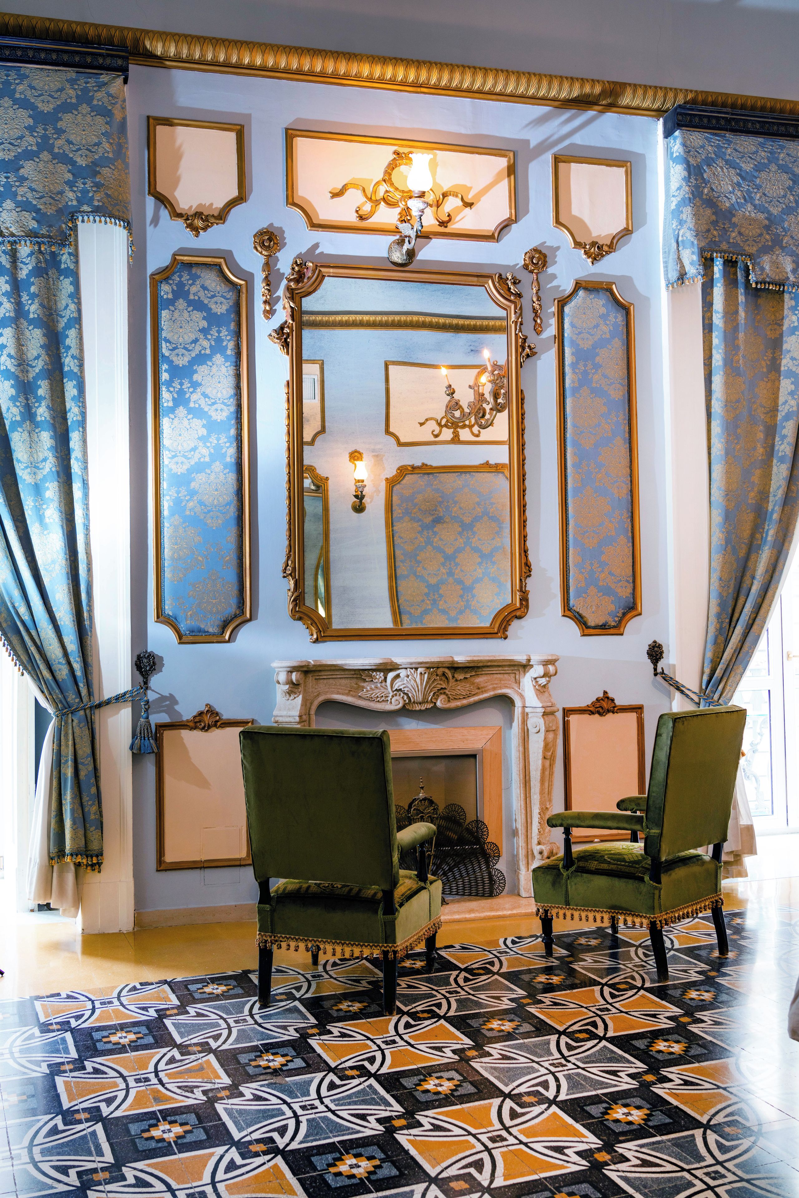 Una stanza con specchi dorati decorati, un camino e due poltrone rivestite di verde.