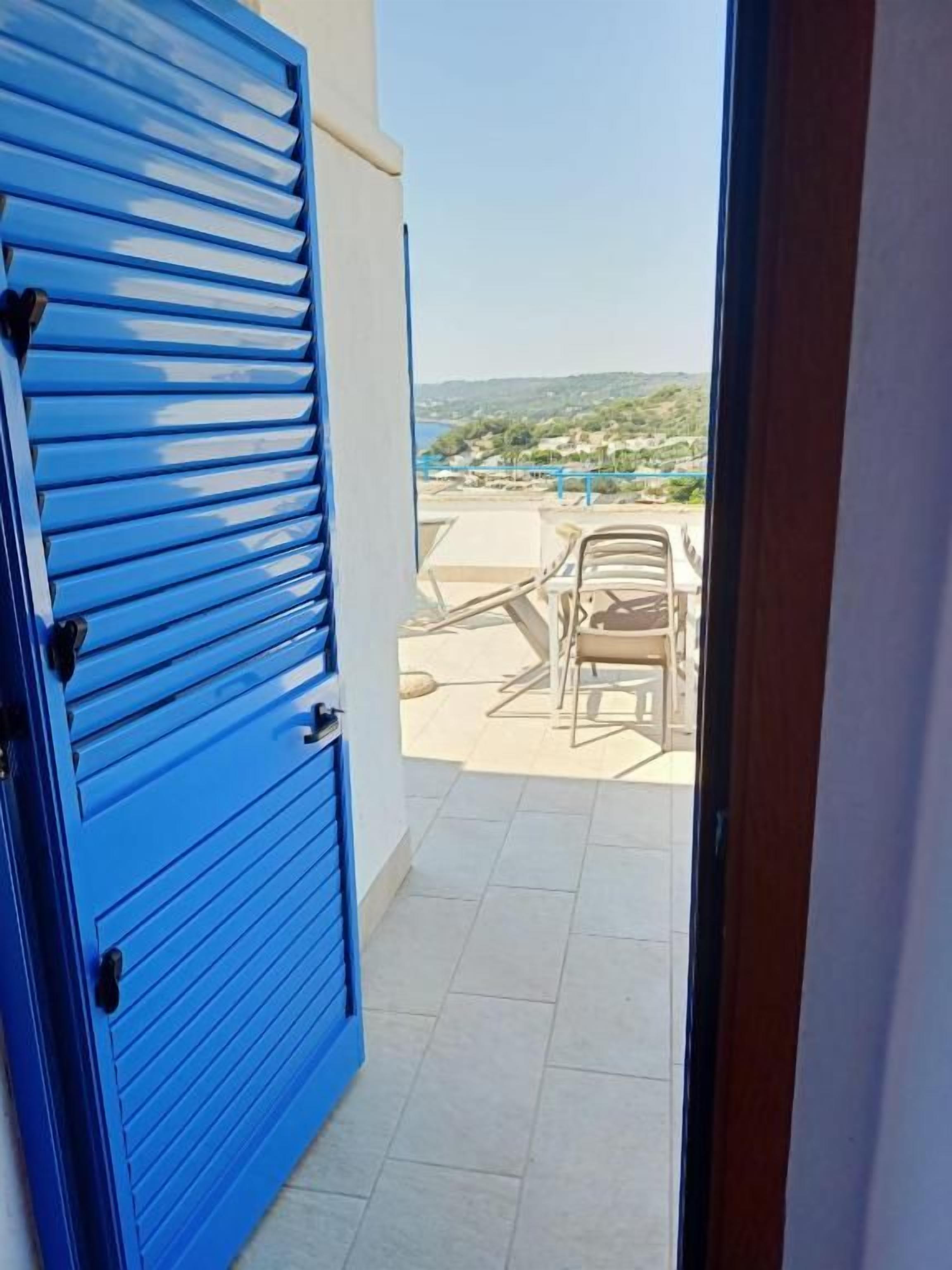 Uma porta azul que dá para uma varanda com vista para uma paisagem distante.