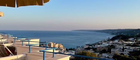 A terrace with a view of the sea, a lounge chair, and a large umbrella.