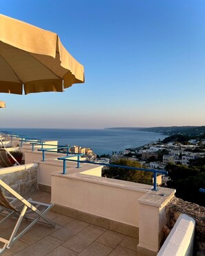 A terrace with a view of the sea, a lounge chair, and a large umbrella. - Hotel Degli Ulivi (Castro)