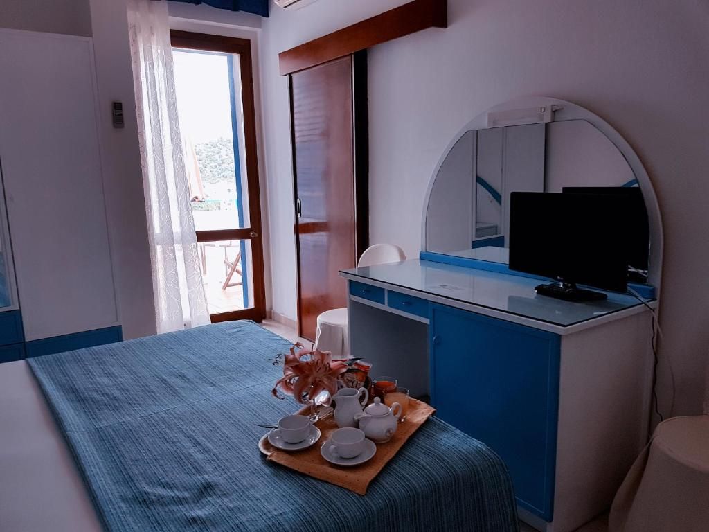 A hotel room with a bed, a desk with a computer, a mirror, and a window.