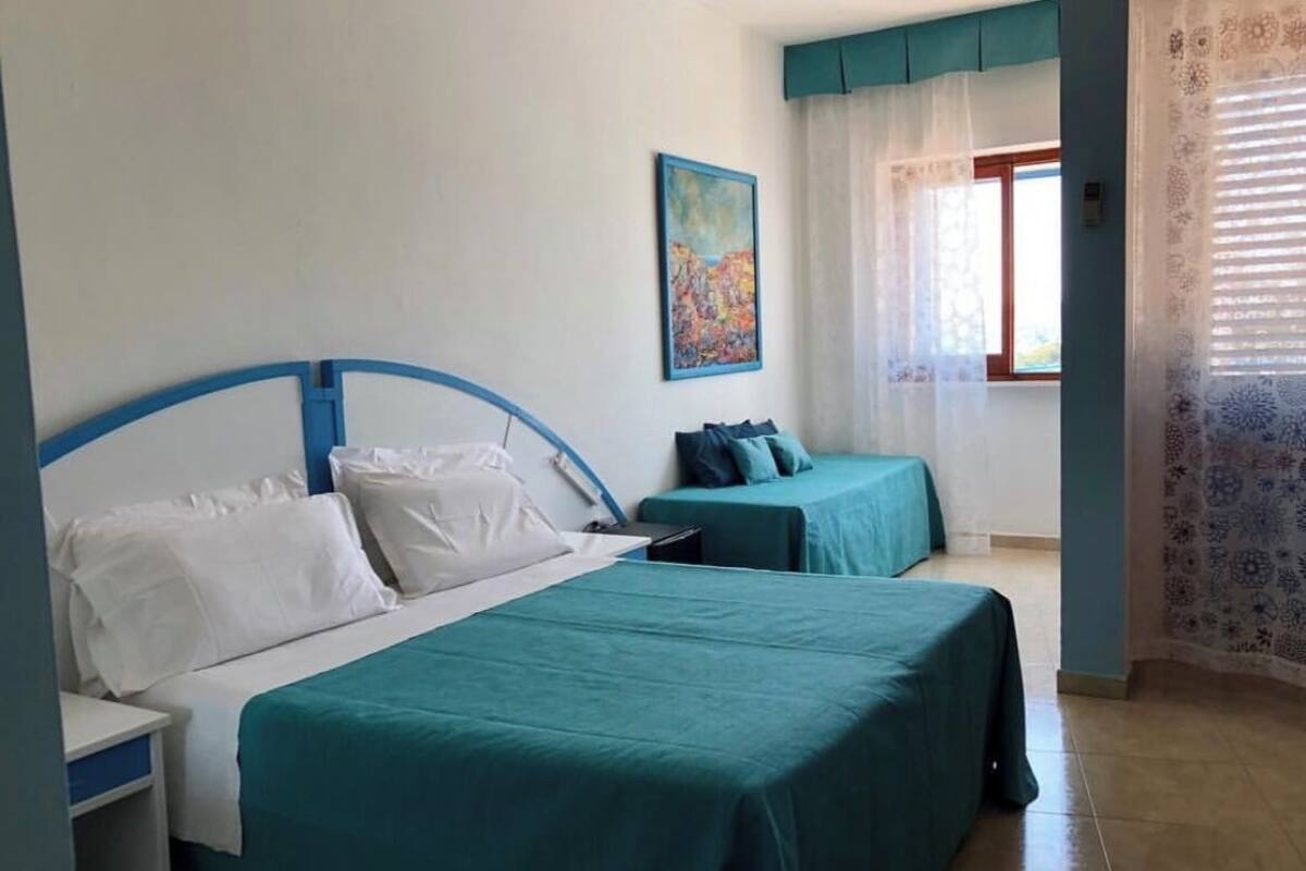A bedroom with two beds, a painting on the wall, and a window with curtains.