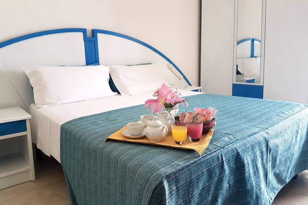 A neatly made bed with white and blue bedding, a tray with breakfast items, and a mirror on the wall.