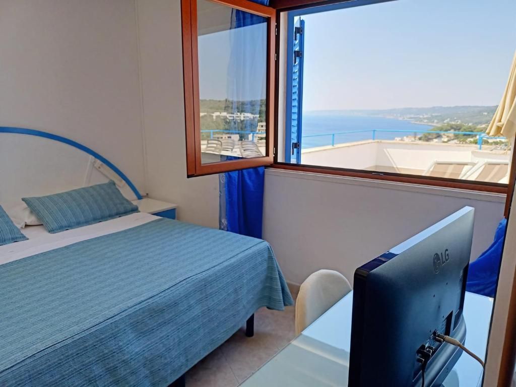 Ein Zimmer mit einem Bett, einem Schreibtisch mit Computer und einem Fenster mit Meerblick.