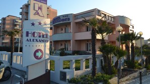 A hotel named 'Hotel Alexander' with a reception area, a sign indicating 'Aperto Tutto l'Anno', and a modern architectural design with balconies and palm trees. - Mia Hotel Numana (Numana)