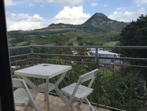 A balcony with a table and chairs, overlooking a mountainous landscape with a building in the distance. - Hotel Magda (Novafeltria)