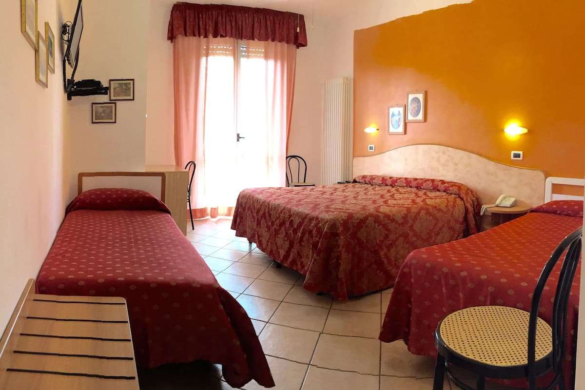 A hotel room with two single beds, a sitting area with a chair, a small table, and a window with curtains.