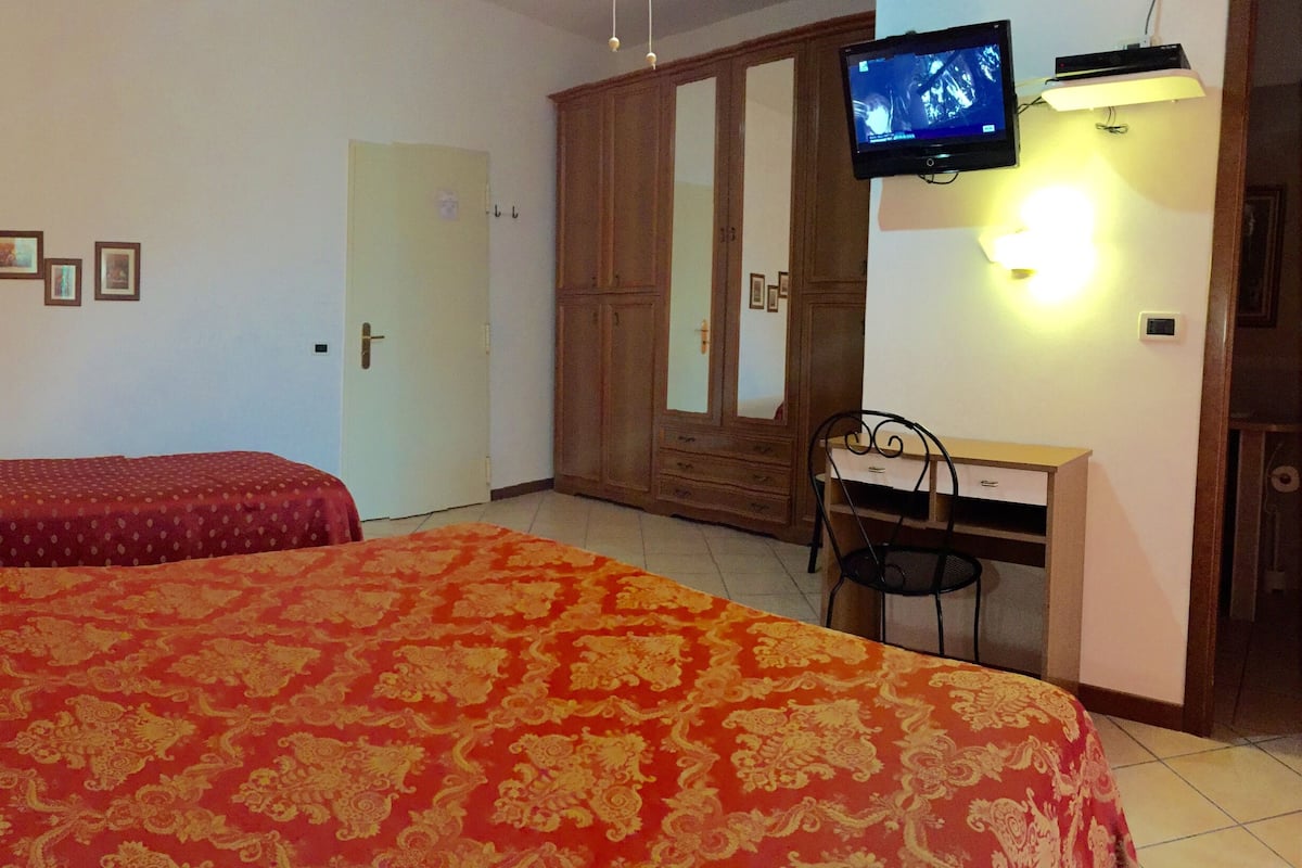 A hotel room with two beds, a wardrobe, a television, and a desk.