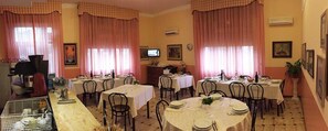 A dining area with multiple round tables, chairs, and pink curtains. - Hotel Magda (Novafeltria)