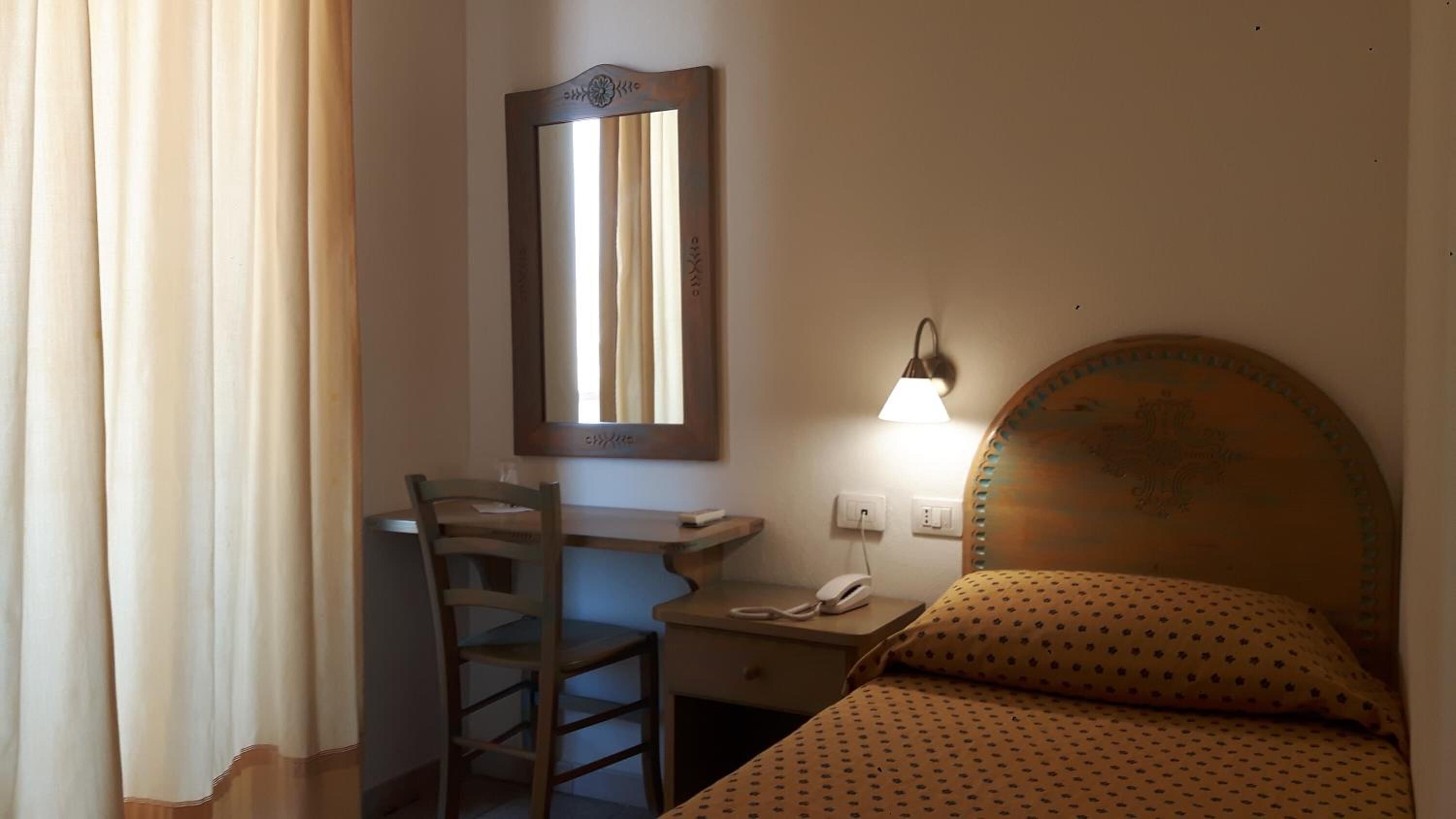 Um quarto pequeno e simples, com uma mesa, cadeira e cama.