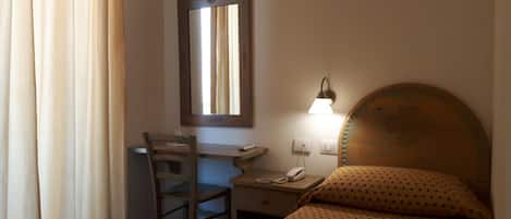 A small, simple room with a desk, chair, and bed.