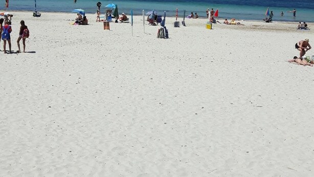 Una playa con gente tomando el sol y nadando.