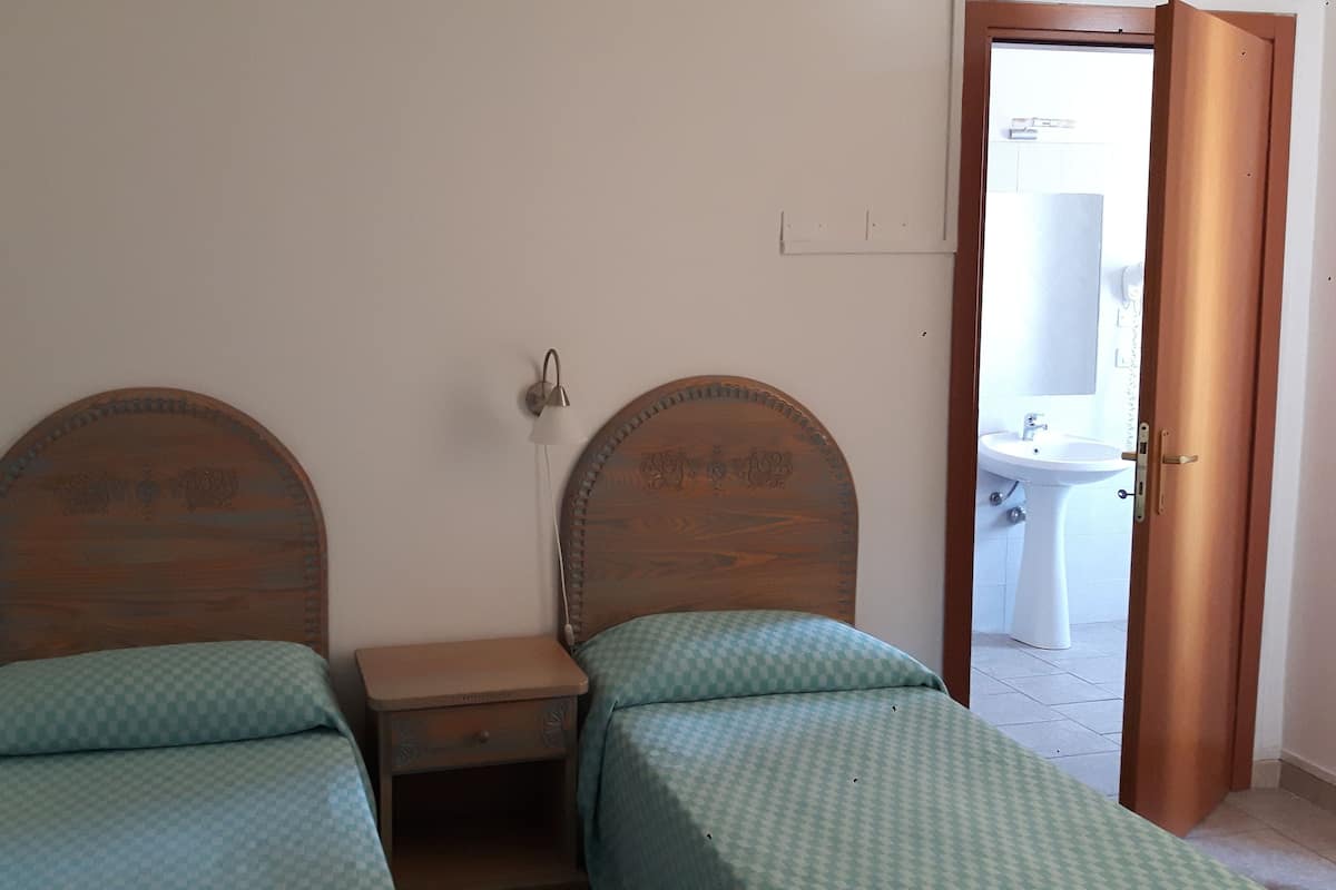 A bedroom with two wooden beds, a small bedside table, and a door leading to a bathroom.