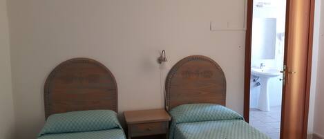 Un dormitorio con dos camas de madera, una mesita de noche pequeña y una puerta que da a un baño.