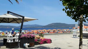 Un café frente a la playa con terraza, una palmera y vistas al mar y a las montañas.