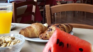 Una mesa de desayuno con croissants, sandía y una manzana.