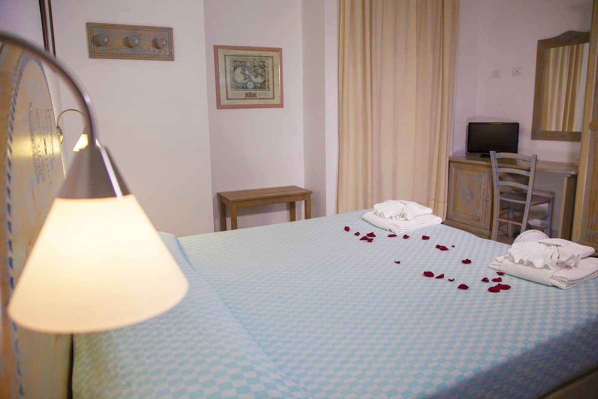 A hotel room with a bed, a desk, a chair, a television, and a lamp.