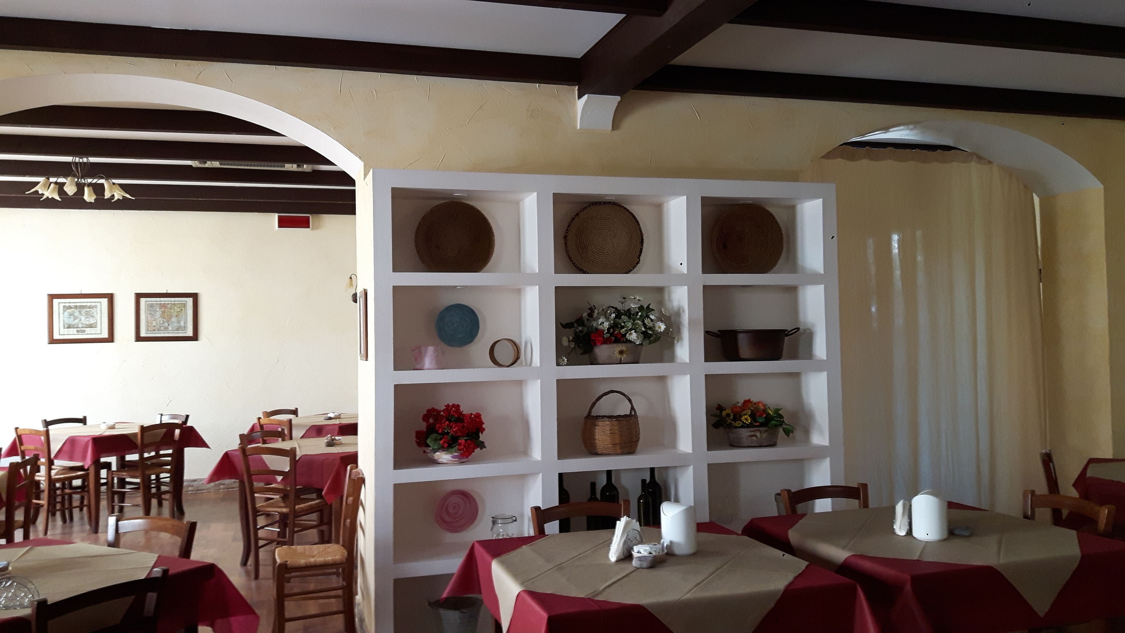 Un comedor con mesas cubiertas con manteles rojos, sillas de madera y un aparador blanco con diferentes utensilios de cocina.