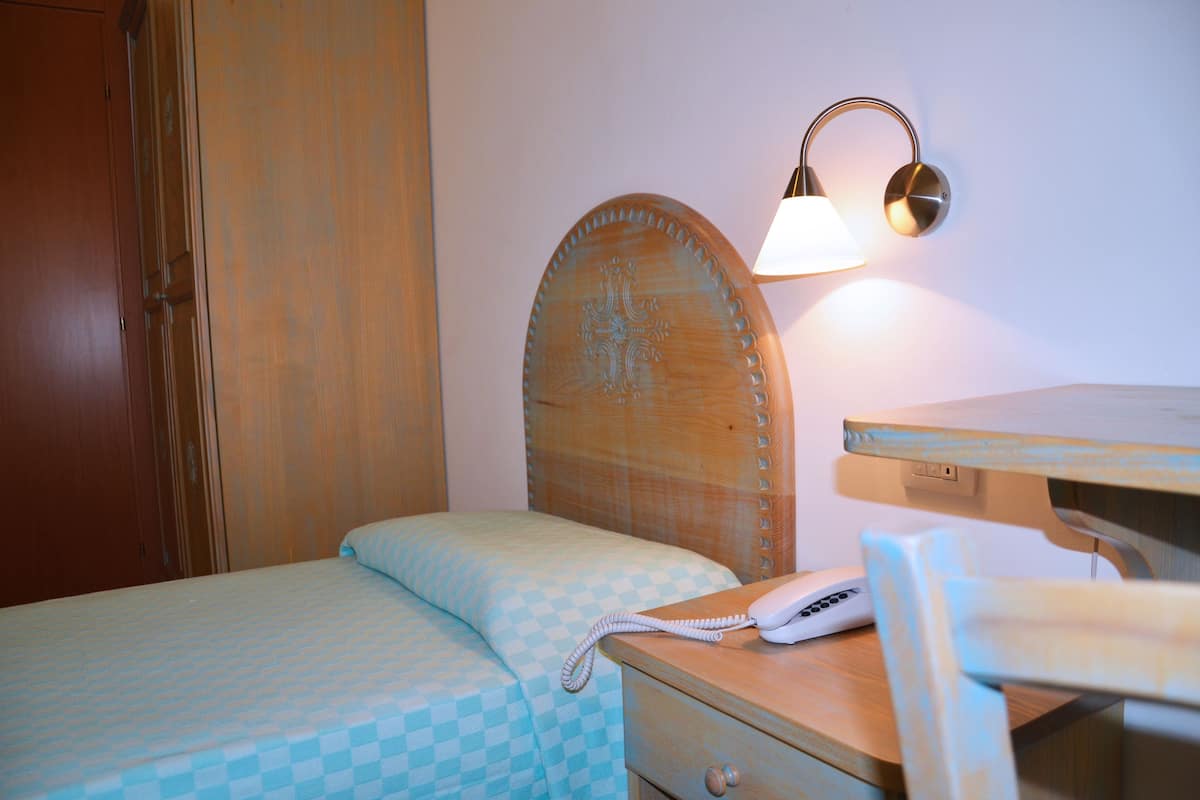 A bedroom with a wooden headboard, a bedside table with a lamp, a telephone, and a bed with a checkered bedspread.