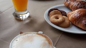 Un desayuno con una taza de café, un vaso de jugo de naranja, croissants y una bandeja de pasteles.