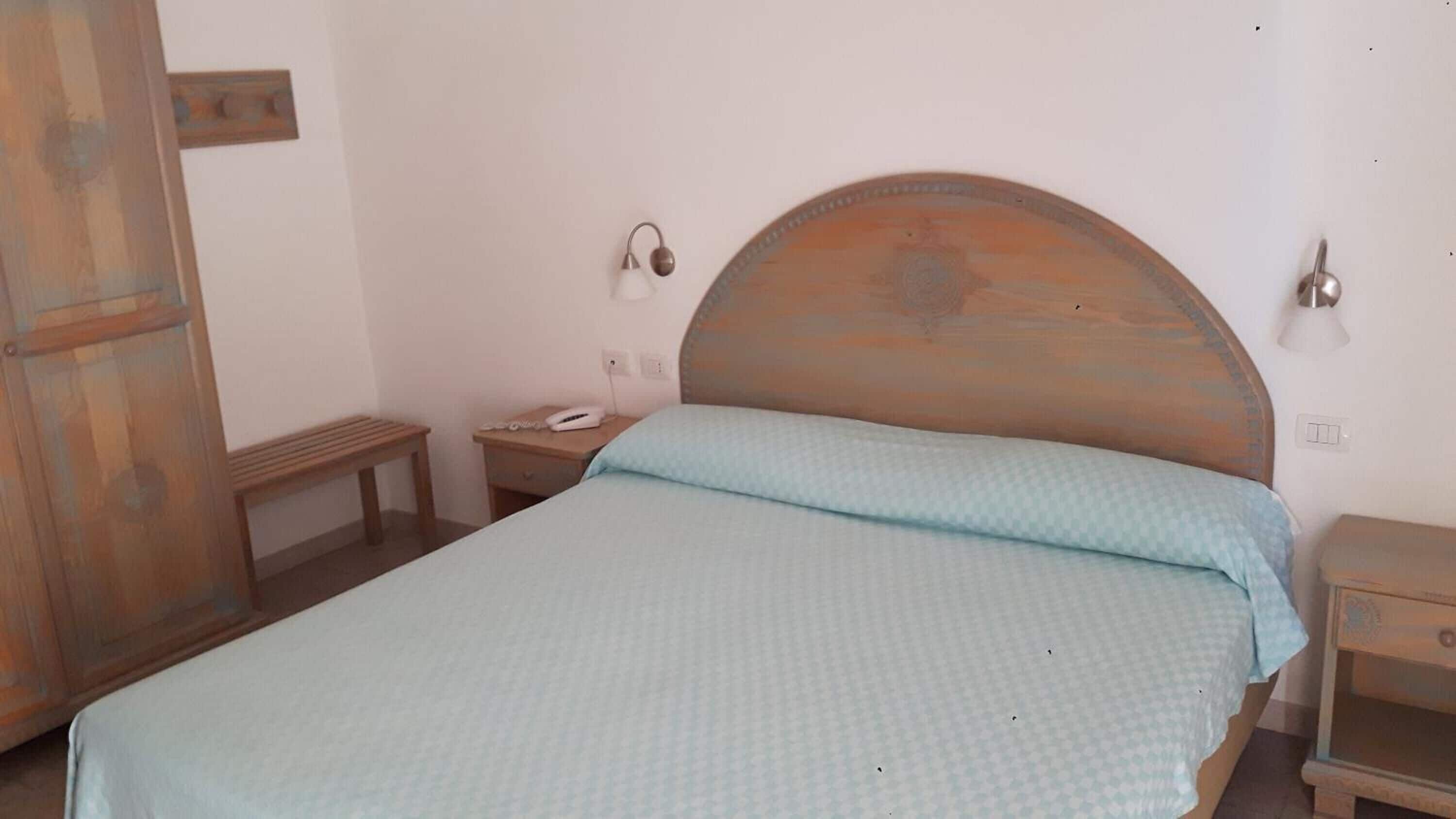 Ein Einzelbett mit Holz Kopfteil, ein Nachttisch mit Lampe und eine kleine Holzbank.