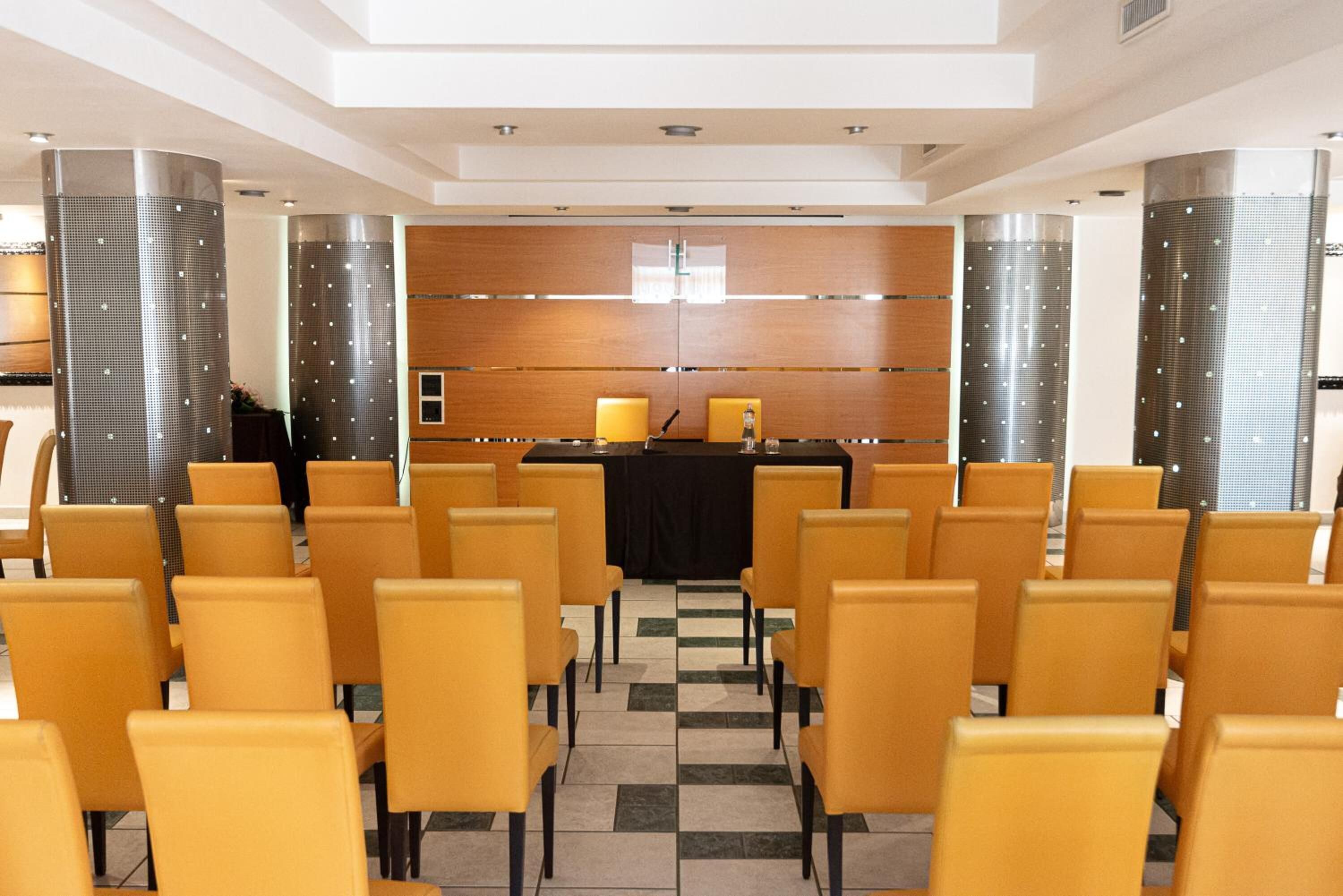 Une salle de conférence avec une table noire, des chaises jaunes et un mur recouvert de panneaux en bois.