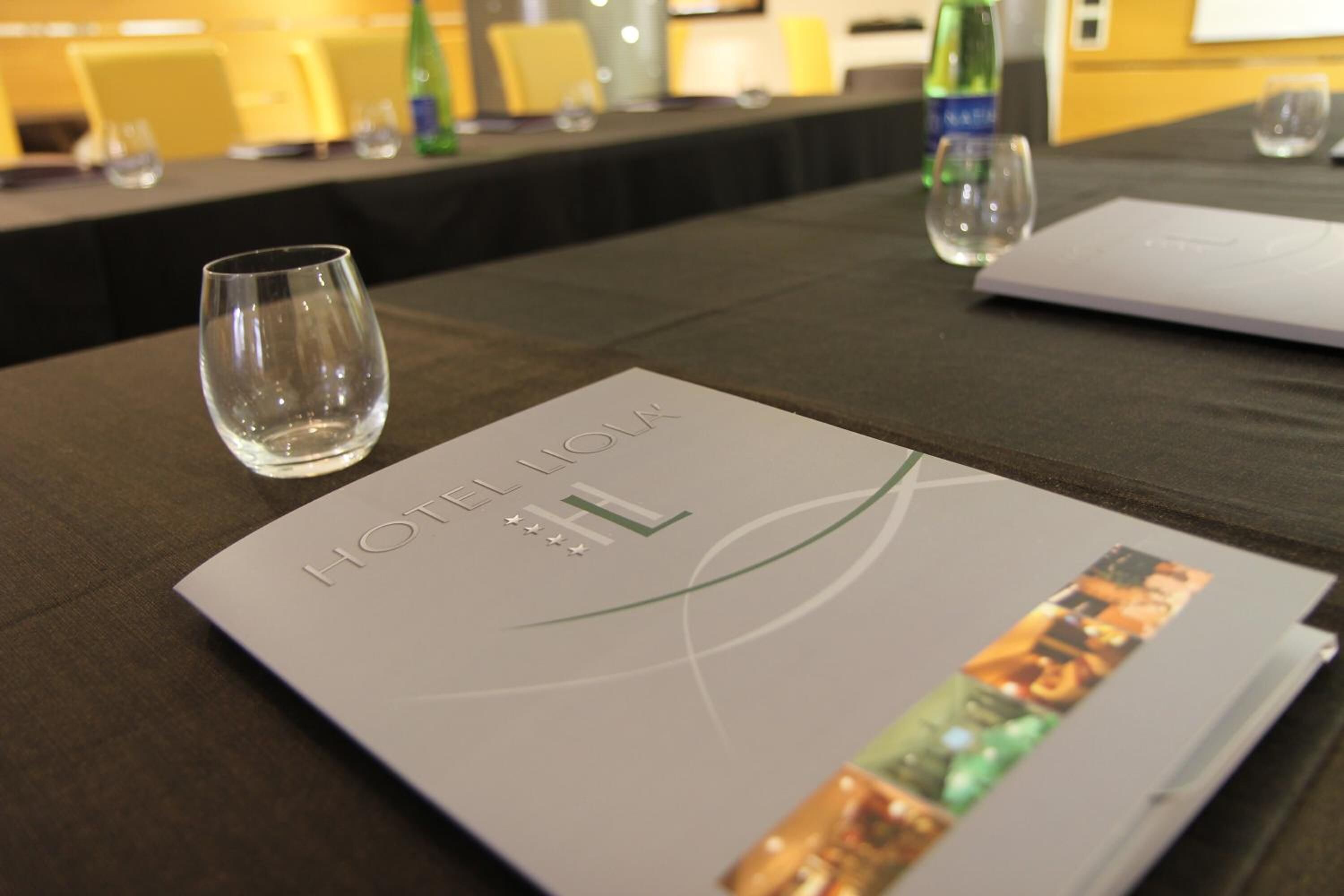 A conference table with a brochure titled "HOTEL LIGA" and a glass of water.