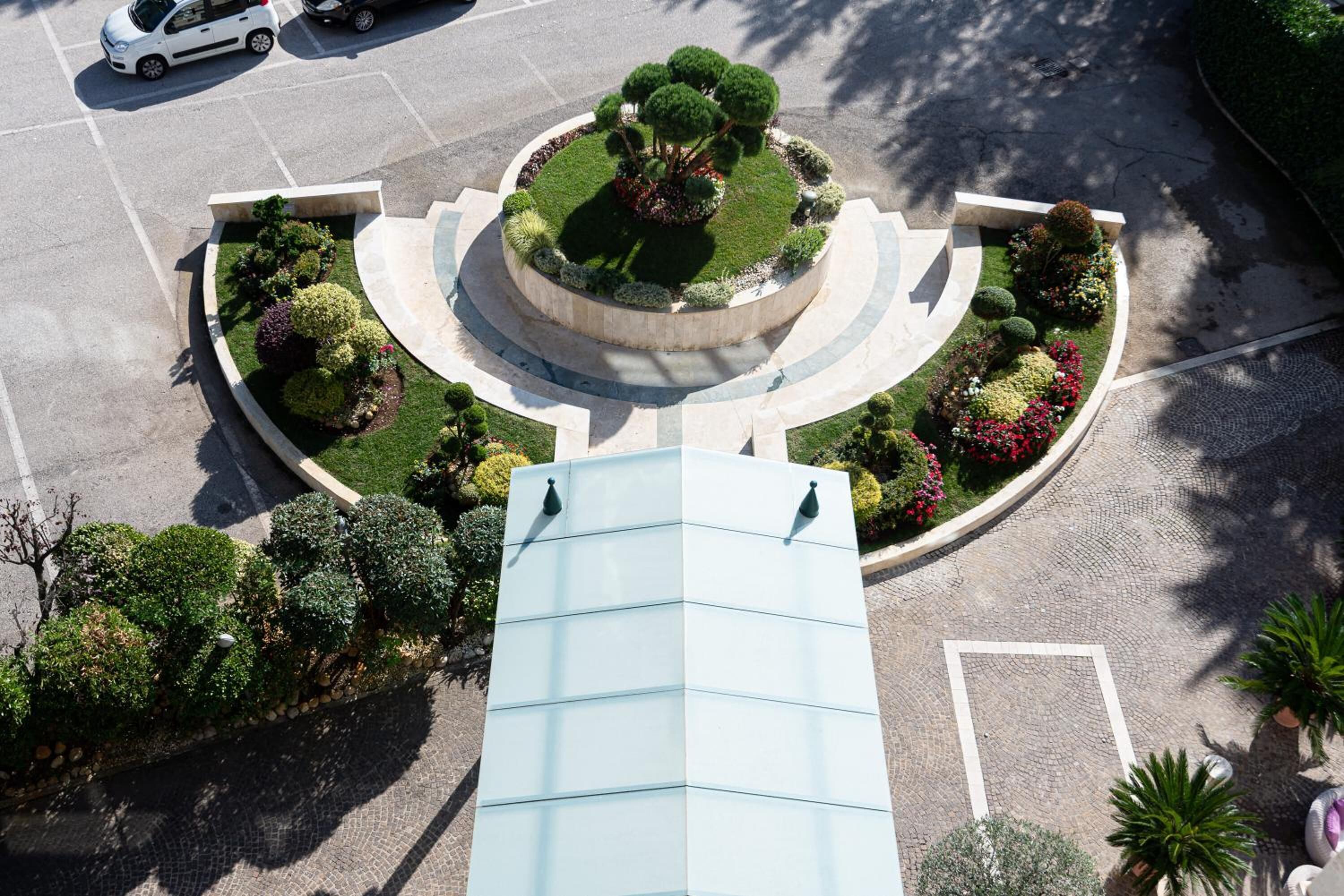 Vue aérienne d’un espace paysager avec un jardin circulaire central, entouré d’un petit muret et agrémenté de diverses plantes.