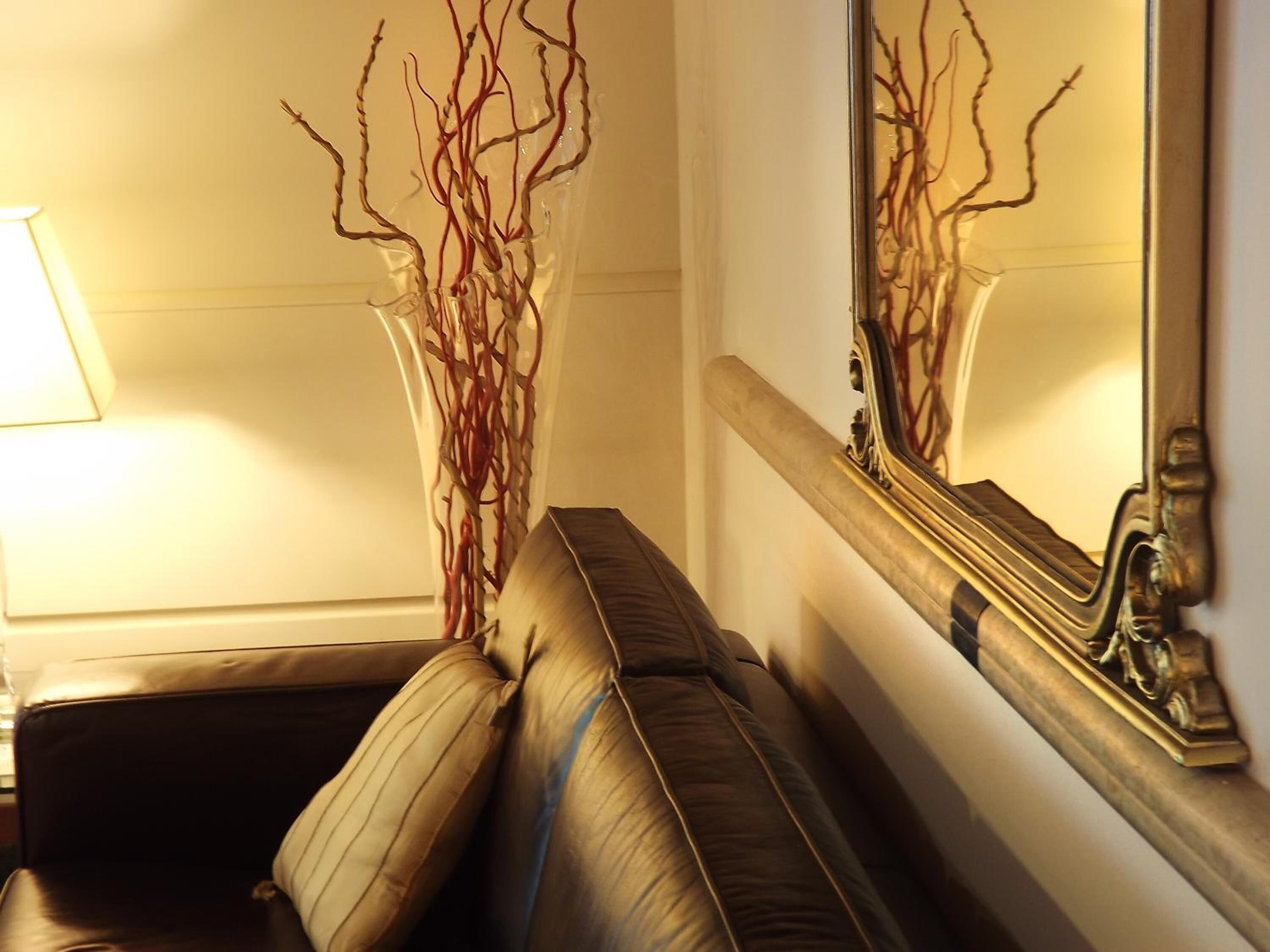 A room with a leather sofa, a tall vase with branches, and a mirror with a gold frame.