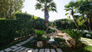 A garden with a stone pathway, palm trees, and various shrubs. - Hotel Liolá (Castrocielo)