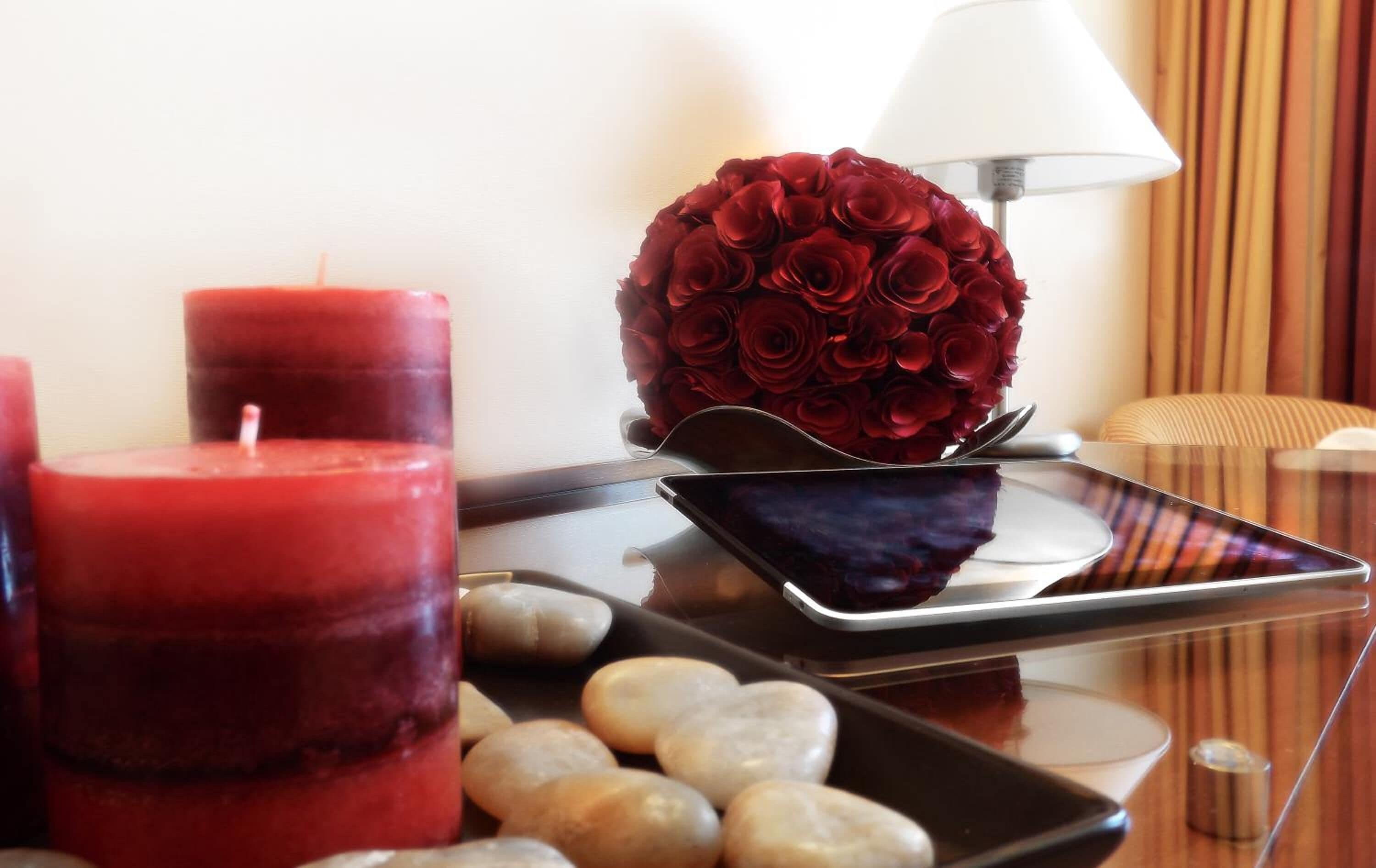 A room with a glass table displaying candles, a rose arrangement, and stones.