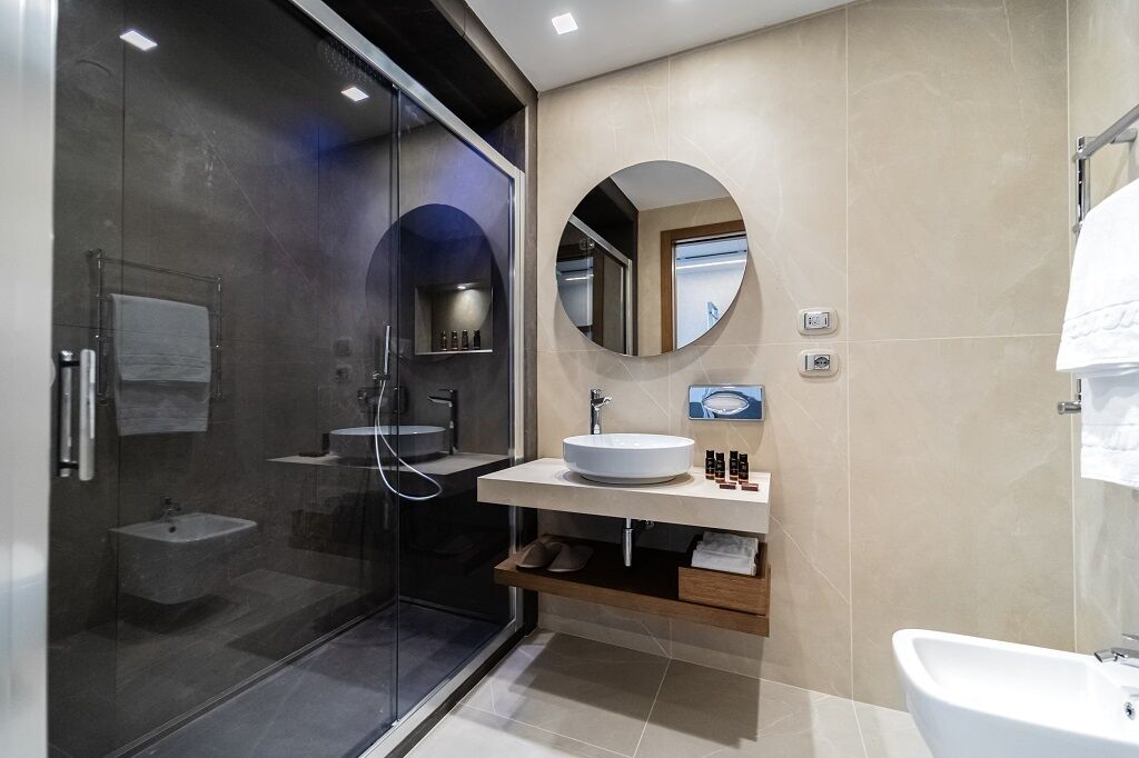 A modern bathroom with a glass shower enclosure, a round mirror, a white sink, and a bathtub.
