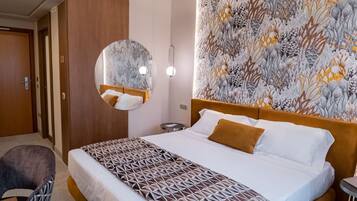 A hotel room with a large bed, a round mirror, a patterned headboard, and a wall with a floral wallpaper design.