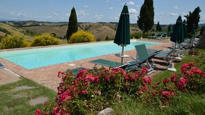 A pool area with lounge chairs and umbrellas, surrounded by flowers and hills in the background. - Podere Benintendi (Certaldo)