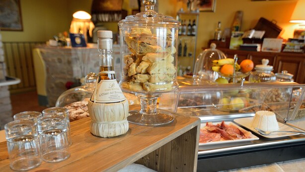 A buffet setup with various food items, a bottle of liquor, and a knife on a wooden table. - Podere Benintendi (Certaldo)