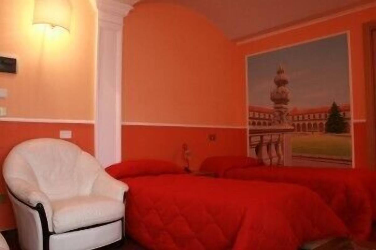 A room with a bed, a chair, and a painting of a building.