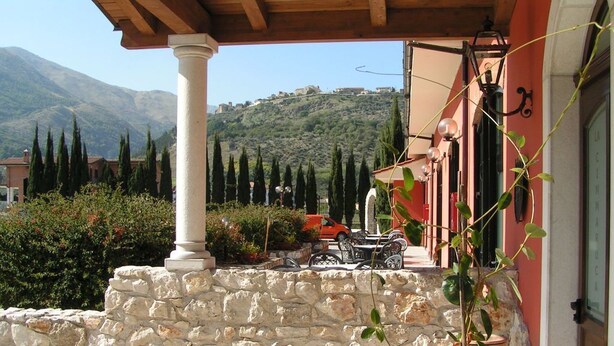 A stone staircase leading to a covered outdoor area with a table and chairs, surrounded by greenery and a mountainous backdrop. - Marchesina Resort (Teggiano)