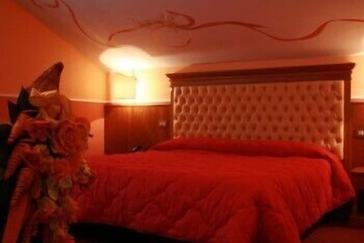 A bedroom with a tufted headboard, a red bedspread, and a nightstand with a lamp.