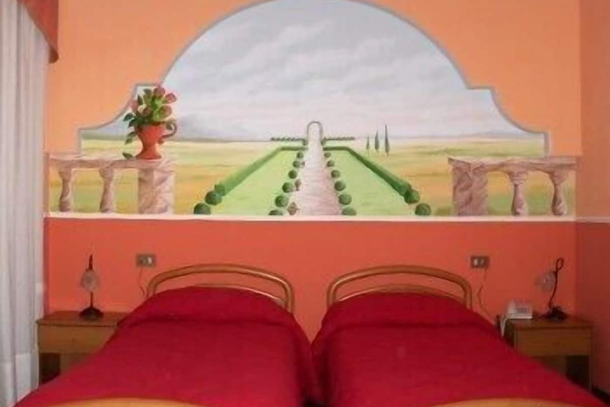 A bedroom with two single beds, a painting of a landscape, and a window with a view of trees.