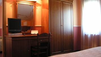 Una habitación de hotel con cama, escritorio con televisor, armario y ventana con cortinas.