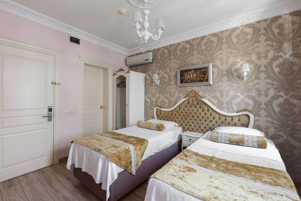 A hotel room with two beds, a chandelier, a painting on the wall, and a door.