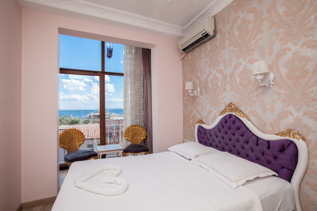 A bedroom with a large bed, a view of the sea, and a balcony with two chairs.
