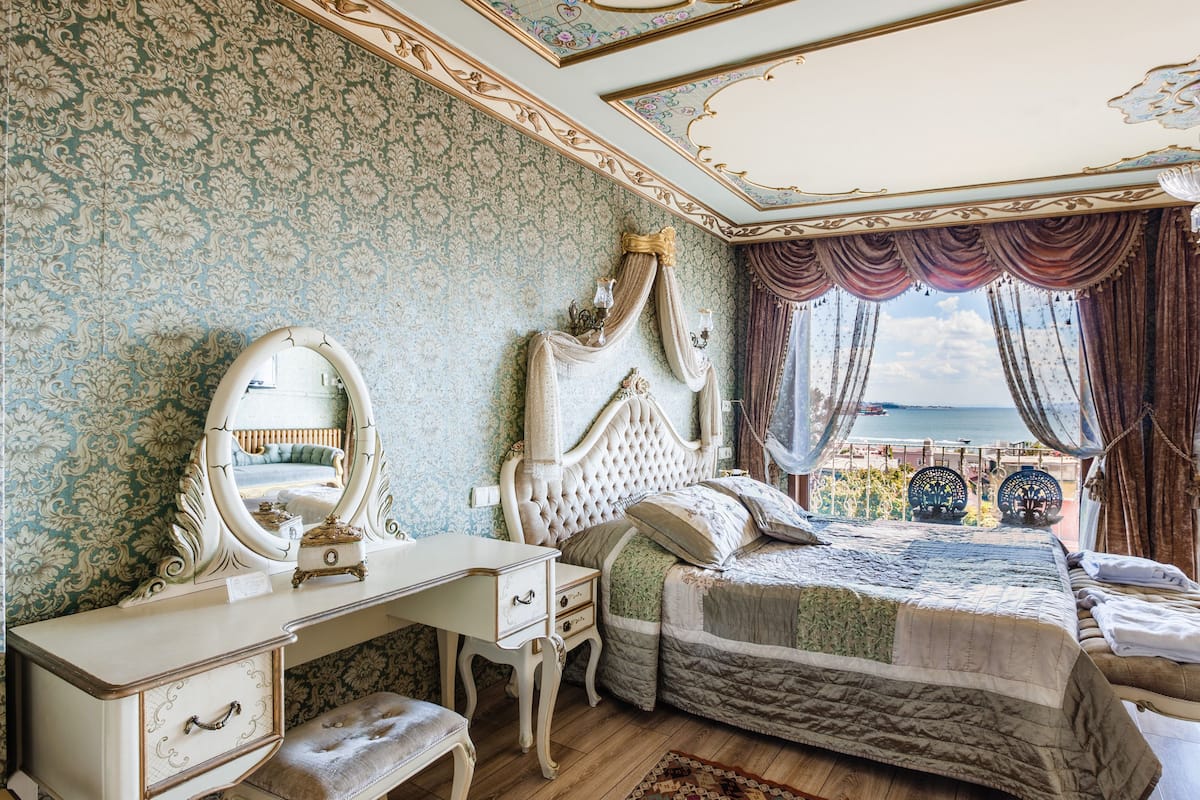 A bedroom with a large bed, a vanity with a mirror, and a view of the sea.