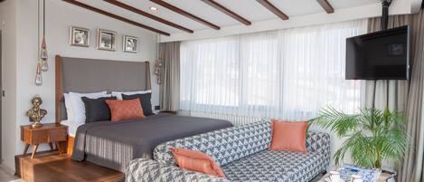 A modern hotel room with a large bed, a sofa, a TV, and a potted plant.